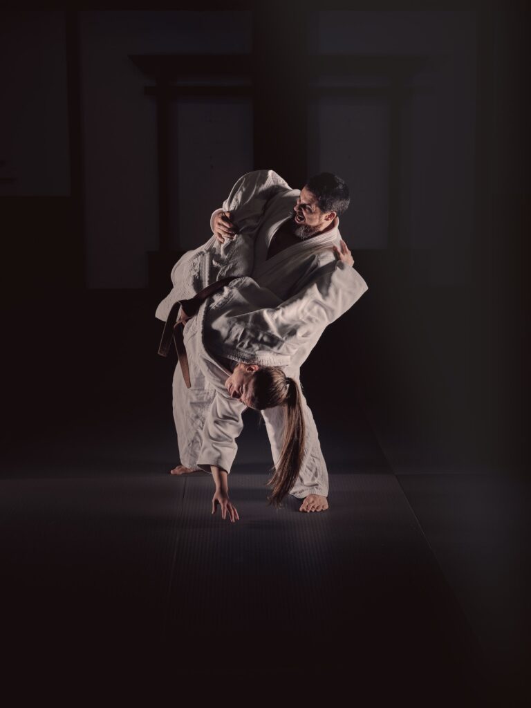 Young judo practitioners showing sweeping hip throw technique in black studio